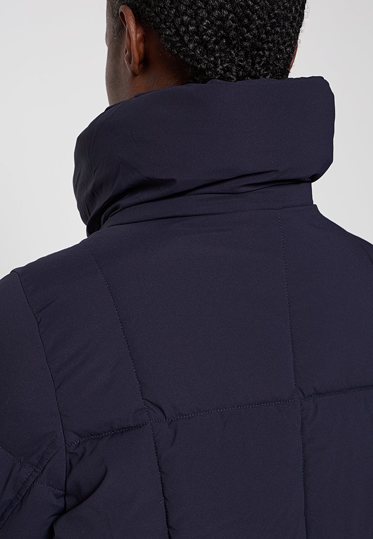 Giubbotto piedi d'anatra blu navy con colletto alto, design trapuntato e texture liscia. La vista dal retro mostra i dettagli delle cuciture e delle cuciture.