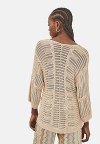 Suéter de punto beige de corte holgado, con mangas anchas y un patrón de tejido abierto. El dobladillo acanalado añade textura al diseño sencillo.