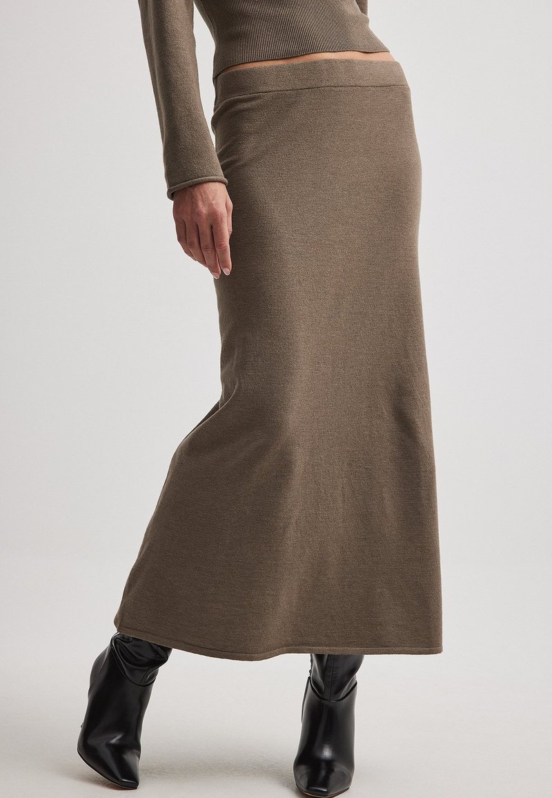 Jupe maxi moulante en tricot côtelé marron à taille haute, associée à un haut à manches longues et des bottes noires jusqu'aux genoux. Texture lisse.