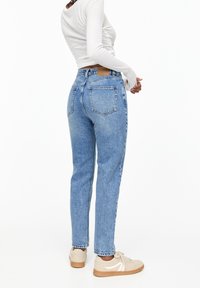 Světle modré džíny s rovnými nohavicemi a vysokým pasem, s dvěma zadními kapsami a světle hnědou koženou nášivkou, doplněné béžovými teniskami.