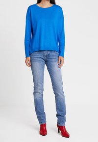 Blauwe lange mouwen trui met een ronde hals, gecombineerd met lichtblauwe jeans en rode hoge hakken. Gladde textuur, casual pasvorm.