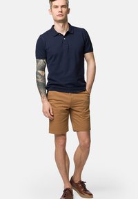 Granatowa koszulka polo i khaki szorty. Polo ma kołnierzyk i krótkie rękawy. Brązowe buty dopełniają strój. Prosty, bez wzorów.