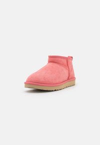 Bottines courtes en daim rose pâle avec un bout rond et un design minimaliste, dotées d'une semelle en caoutchouc et d'un petit élastique latéral pour un enfilage facile.