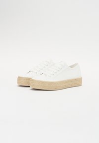 White canvas sneakers with a textured woven jute platform, featuring a rounded toe, lace-up design, and subtle stitching details.