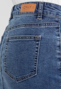 Höga blå denimjeans med en läderpatch med "ONLY"-logotyp, med bakfickor och en slät textur.