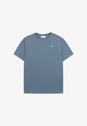 T-shirt blu a maniche corte con scollo rotondo, con piccolo logo rosa a forma di albero sul petto a sinistra e un'etichetta bianca sul colletto.