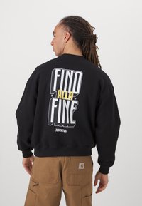Svart hettegenser med en dristig grafikk i hvit og gul tekst på baksiden, med ordene "FIND ALLA FINE" og "JUVENTUS". Laget av en blanding av bomull.