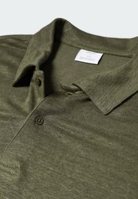 Olivgrünes Poloshirt mit zwei braunen Knöpfen und umgeschlagenem Kragen, flach ausgelegt mit sichtbarem weißen Markenetikett innerhalb des Kragens.