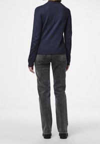 Pull bleu marine à manches longues, col et ourlet côtelés. Associé à un jean gris texturé taille haute et des chaussures noires.