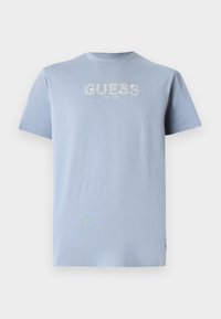 Vaaleansininen puuvillapaita, jossa on lyhyet hihat ja pyöreä kaula-aukko. Edessä valkoinen logotuloste "GUESS EST. 1981". Sujuva pinta.
