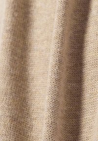 Beige gebreide stof met een fijne, zachte textuur. Het patroon toont subtiele variaties in kleur en dikte door het materiaal heen.