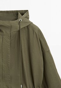 Olivgrüne Kapuzenjacke mit Kordelzug und Metallösen, mit sichtbaren Nahtnähten und glatter Stoffstruktur.