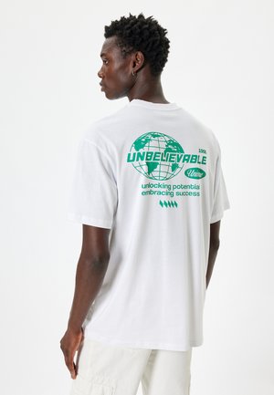 Hvid bomulds T-shirt med grøn grafisk print med globusdesign og tekst på ryggen. Korte ærmer, afslappet pasform og rund hals.