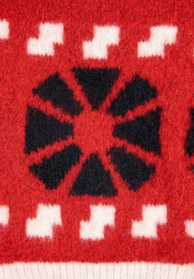 Rote Strickware mit einem großen schwarzen Blumenmuster, das aus dreieckigen Blütenblättern und weißen Akzentformen besteht. Weiche Textur und einheitliches Design.