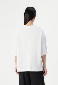 Witte oversized T-shirt met korte mouwen, voorzien van een ronde hals en een naaddetail aan de achterkant. Glad textuur, gemaakt van lichtgewicht stof.