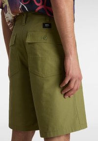 Olivengrønne cargo shorts i slidstærkt stof, med to baglommer, et VANS-mærke og en lige pasform med synlige syninger.