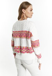 Fehér cable-knit pulóver, különböző színű geometrikus mintákkal rózsaszín, sárga és kék csíkokban. Kerek nyakkivágással és bordás mandzsettákkal rendelkezik.