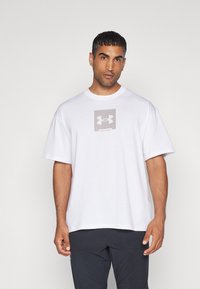 Hvid bomulds t-shirt med korte ærmer, der har et gråt kvadratisk logo på brystet. Enkelt, afslappet pasform design.