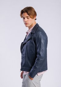 Chaqueta de motocicleta de cuero navy con un diseño ajustado, cierre de cremallera asimétrico y una textura suave; combinada con una camisa de color rosa claro.