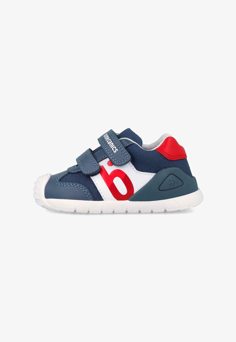 Zapatilla para niño pequeño en azul marino y blanco con detalles en rojo, dos correas de velcro y suela blanca, vista lateral.
