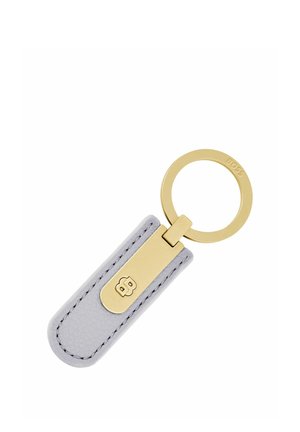 Porte-clés en métal doré attaché à une étiquette en cuir gris avec des bords cousus et un logo embossé.