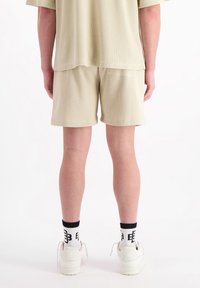 Lichtbeige, gebreide shorts met textuur en een ontspannen pasvorm, voorzien van een achterzak, gecombineerd met witte sneakers en sokken met zwarte accenten.