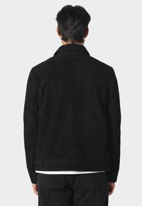 Černá semišová bunda s klopovým límcem, hladkou texturou a rovným střihem. Na zadní straně nejsou viditelné žádné kovové prvky ani vzory.