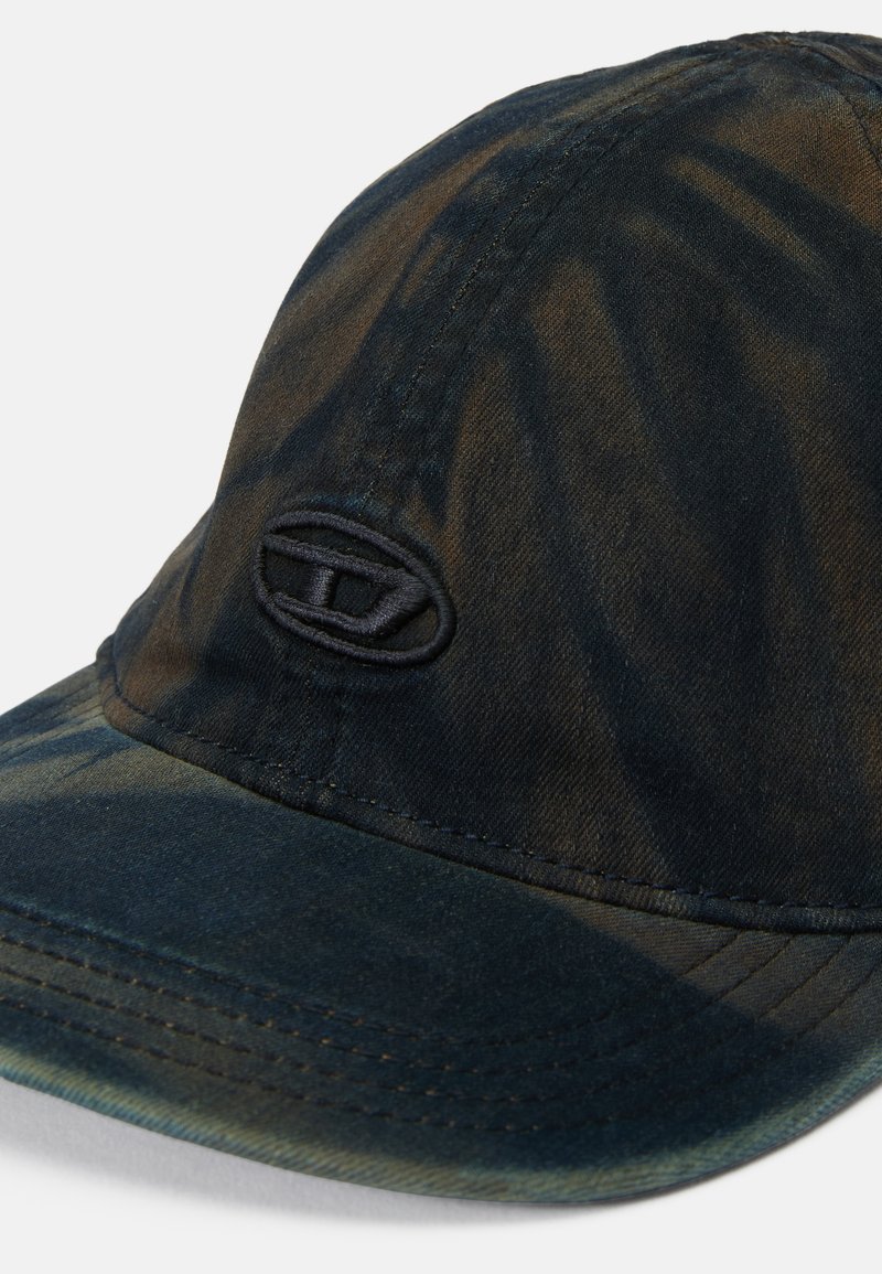 Casquette en tissu sombre avec un motif tie-dye dans des teintes de bleu et de marron. Présente une surface texturée et un logo brodé sur le devant.