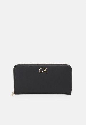 Portafoglio nero con zip realizzato in materiale liscio, caratterizzato da un logo "CK" dorato sul fronte. Forma rettangolare con un design minimalista.