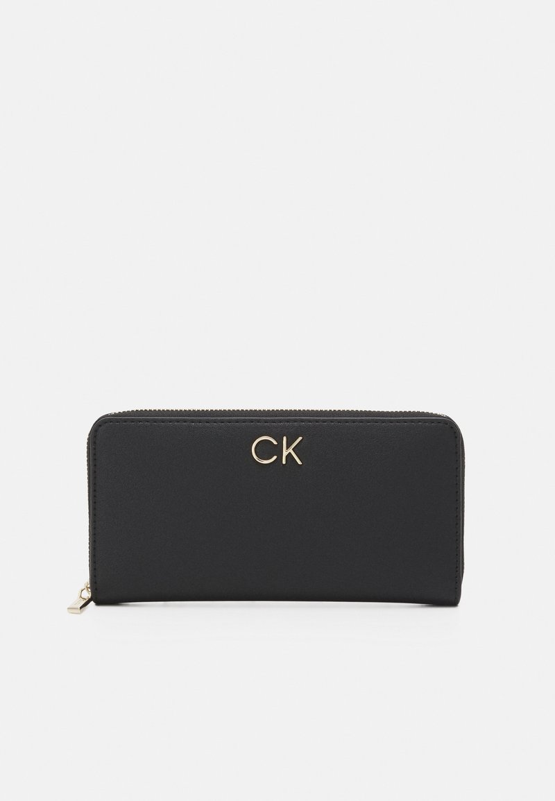 Portafoglio nero con zip realizzato in materiale liscio, caratterizzato da un logo "CK" dorato sul fronte. Forma rettangolare con un design minimalista.