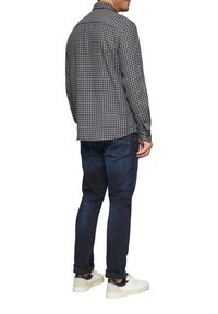 Zwart-wit geblokt overhemd met lange mouwen en een normale kraag, gecombineerd met donkerblauwe jeans en witte sneakers.