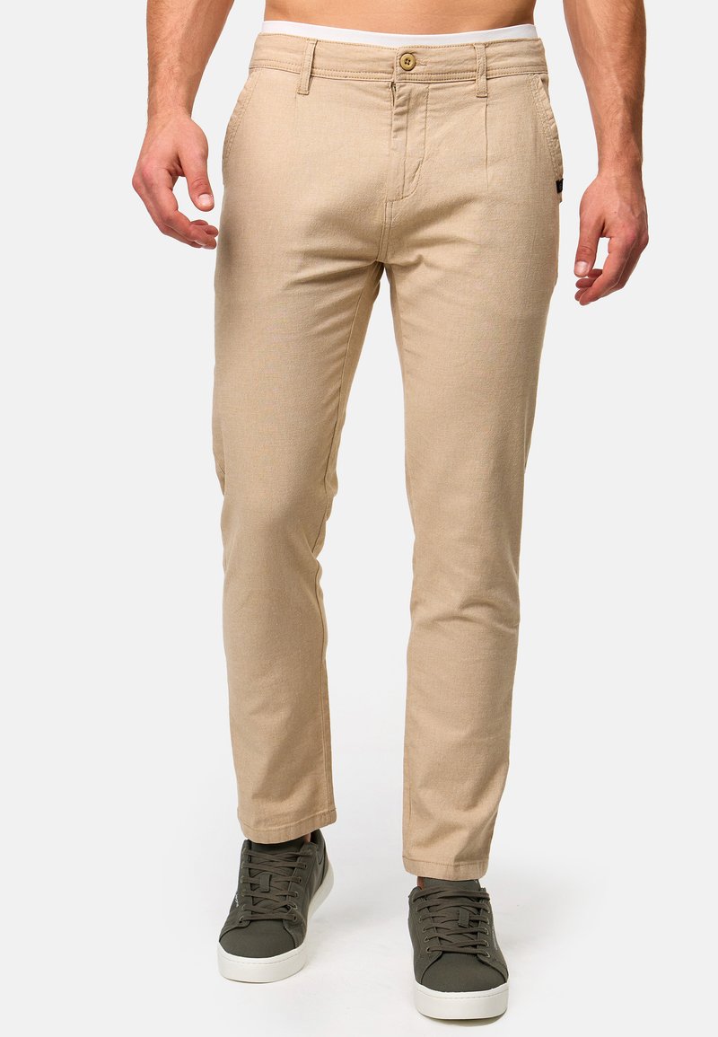 Beige chinos med slim fit, med knappelukking, beltehemper og frontlommer. Kombinert med mørkegrønne sneakers for kontrast.