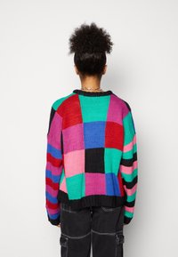 Maglione lavorato a maglia multicolore con un design a patchwork in vivaci tonalità di rosa, blu, verde e nero, con un colletto e un orlo a coste neri.