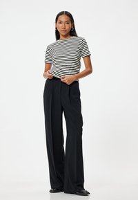 Top de rayas de manga corta en blanco y negro, combinado con pantalones de pierna ancha negros de cintura alta. Tejido suave con un corte relajado.