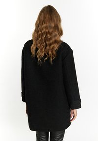 Zwarte textuur jas met brede mouwen en een losse pasvorm, met een middellange ontwerp en opgerolde manchetten. Glad, sleek leren broek zichtbaar.