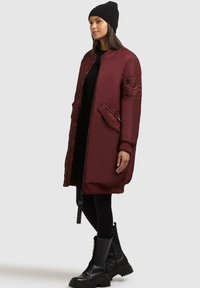 Bordeaux lange bomberjack met gequiltte schouderdetails, zijzakken en ritsluiting, gecombineerd met zwarte leggings en combatboots.