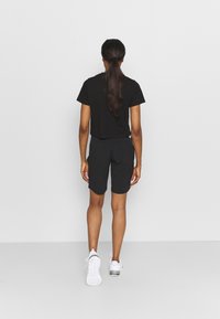 Svart kortärmad t-shirt med korta ärmar, matchad med svarta shorts. Skorna är vita träningstövlar. Håret är långt och rakt, uppsatt.