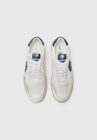 Hvite sneakers med perforert tekstur, marineblå aksenter, flate hvite snørebånd og en rund logo på siden. Lett gummisåle.