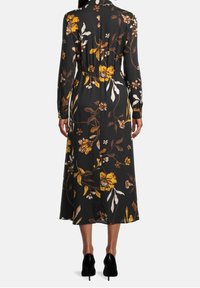 Lång svart klänning med blommönster i gult och brunt, med långa ärmar, midjeband och en svängig nederkant. Bärs med svarta högklackade skor.