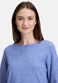 Pull bleu clair avec une finition texturée, coupe ample et encolure large. Tissu doux, manches longues, détails de couture minimes.