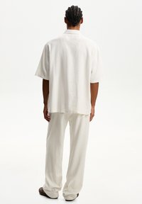 Camisa de lino blanca de manga corta combinada con pantalones blancos de corte holgado. La textura parece ligera y transpirable. Vista trasera sin detalles.