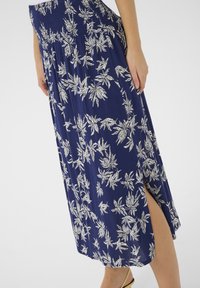 Jupe maxi bleu marine avec imprimé floral blanc, dotée d'une taille smockée et d'une fente sur le côté pour faciliter les mouvements. Tissu doux et texturé.