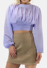 Jasnofioletowa krótka bluzka z długimi, bufiaste rękawy i marszczeniem w talii, zestawiona z beżową mini spódnicą. Gładka faktura.