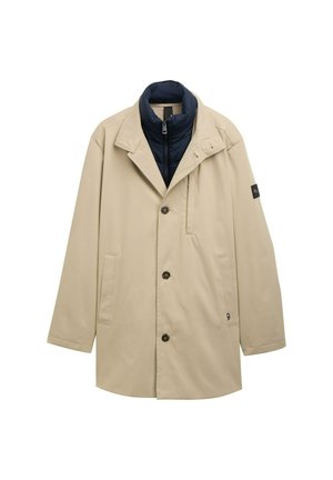 Manteau beige avec un col matelassé bleu, fermeture à boutons croisés, poches latérales et accent noir sur la manche.