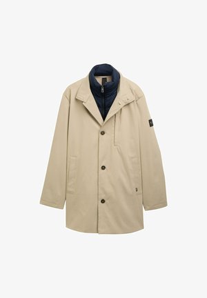 Beżowy płaszcz z niebieską podszewką kołnierza, z jednorzędowym zapięciem na guziki, kieszeniami po bokach i czarnym akcentem na rękawie.