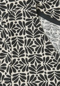 Primer plano de tela en blanco y negro con un patrón abstracto de hojas repetitivo y una costura visible cerca de un borde doblado.