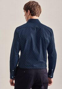 Marineblauw overhemd met lange mouwen en knopen, voorzien van witte stippen, een klassieke kraag en een gladde textuur. Straatmodel met knoopmanchetten.