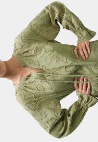 Lichtgroene blouse met bloemenborduursels, lange mouwen, geweven stof en een keyhole-uitsparing. Samengestikte manchetten zorgen voor een gepofte uitstraling.
