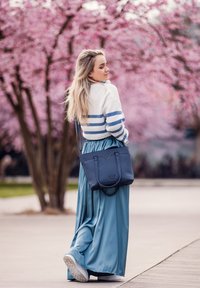 Navy quilted handbag with dual handles, worn with a light blue satin maxi skirt and a white sweater with blue stripes, amid pink blossoms.