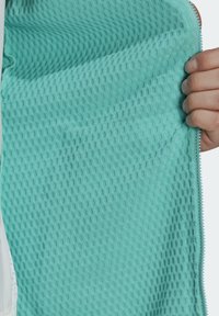 Main tenant un tissu turquoise texturé avec un motif circulaire en relief et des bords cousus.
